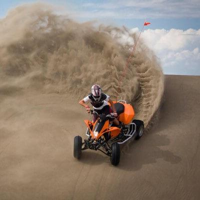 在怀俄明州的Killpecker沙丘上，一名戴着头盔和防护装备的人骑着一辆橙色的沙滩车. 亚视轮胎踢起沙子，在后面形成波浪墙.